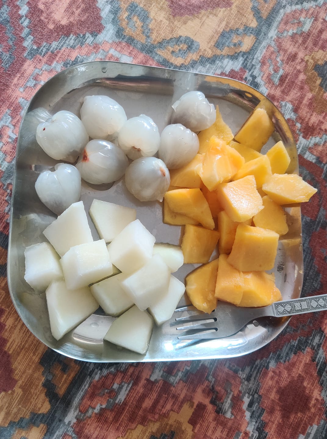 Fruit platter with only orange and white colored fruits on a steel plate with a fork.